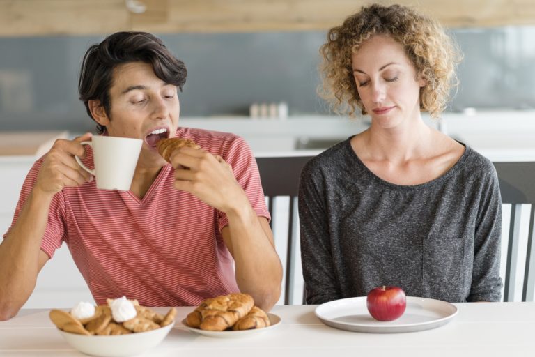 Un homme boit son café avec croissant tandis que sa femme regarde la pomme posée dans son assiette