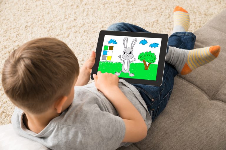 Un enfant dessine un lapin dans l'herbe sur une tablette tactile